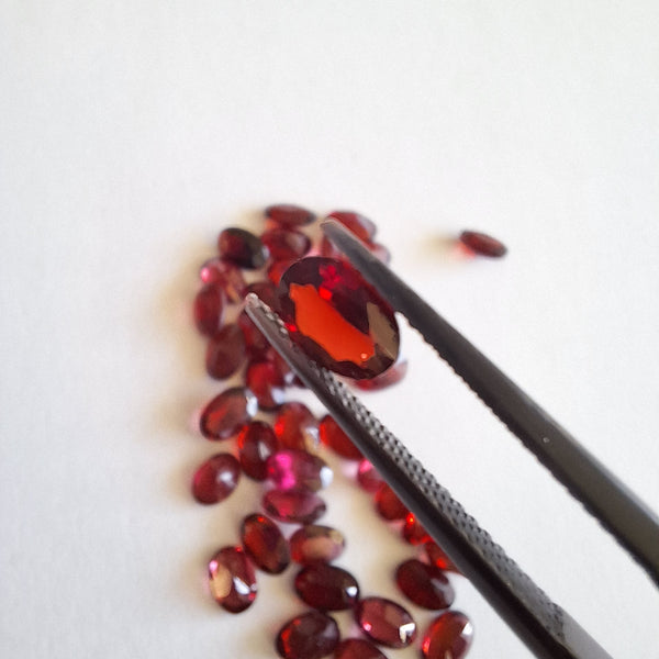 Garnet gemstones with a pair of tweezers on a white background cape diamond exchange,  South Africa