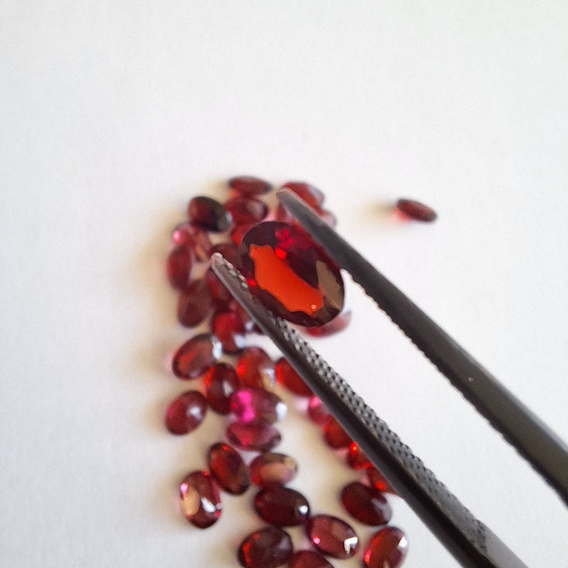 Garnet gemstones with a pair of tweezers on a white background cape diamond exchange,  South Africa