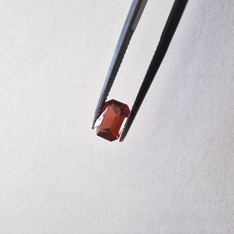 Red gemstone held by tweezers on a light gray background